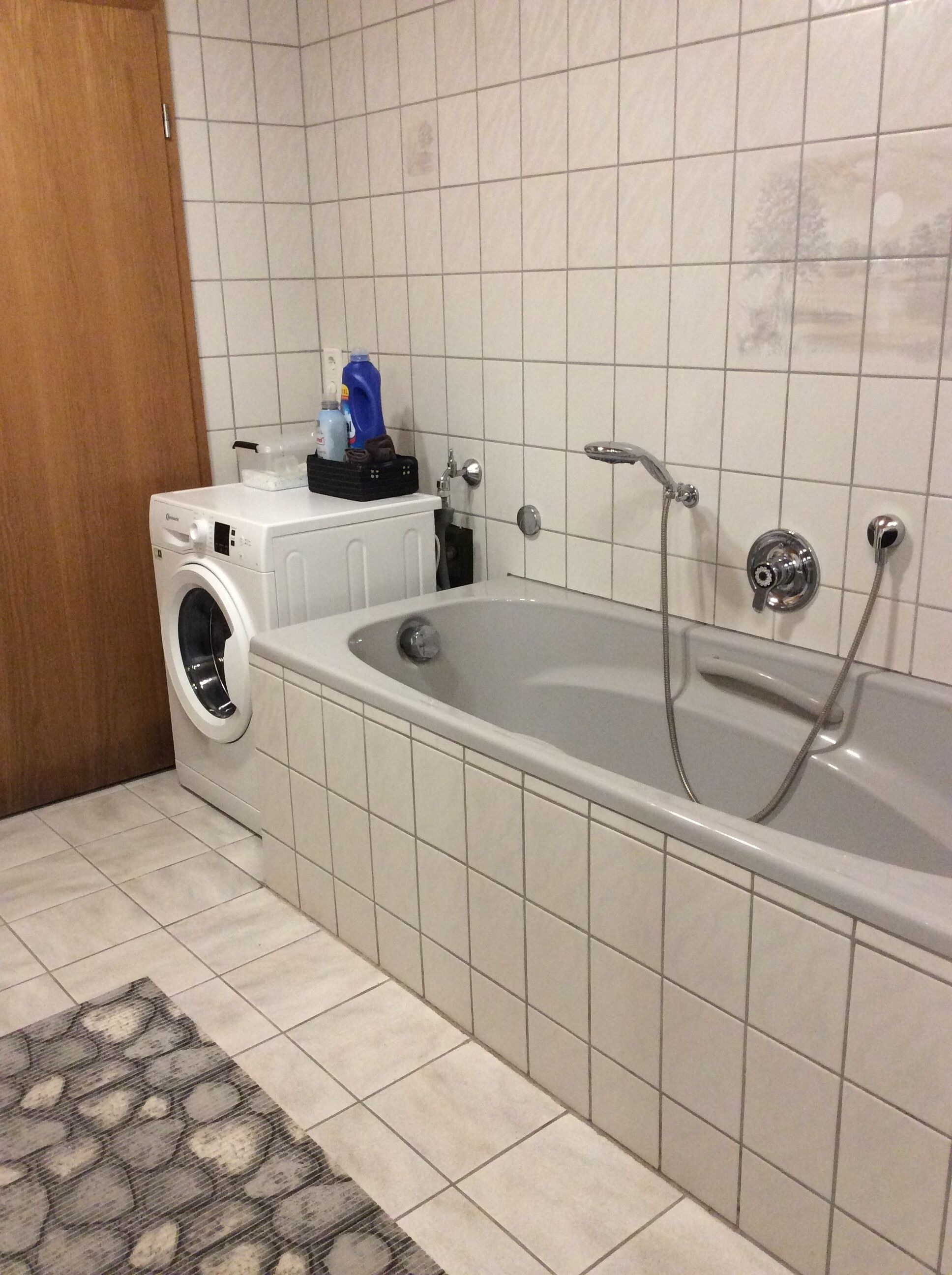 Ett badrum med tvättmaskin, badkar och ett kaklat golv.
