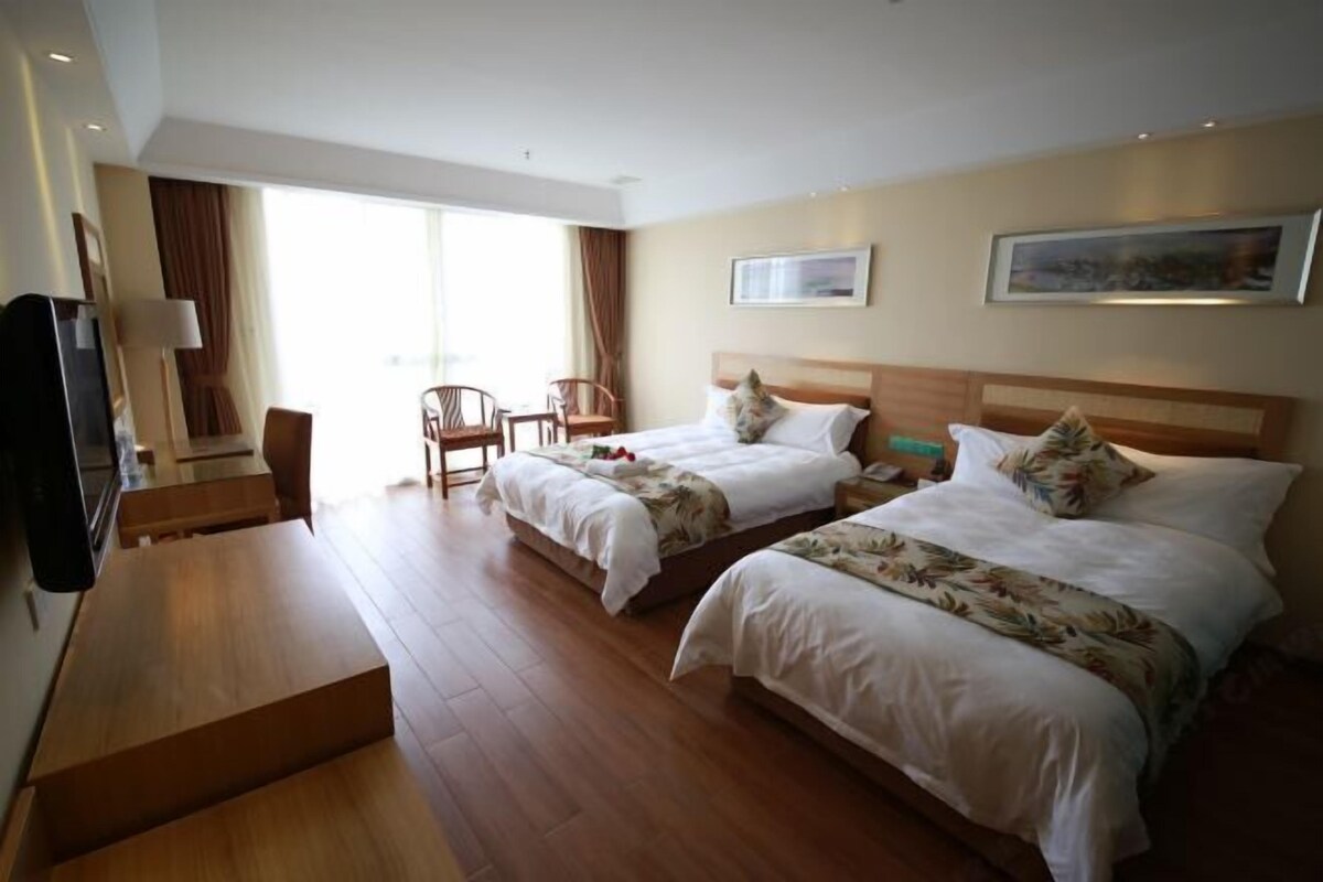 A hotel room with two beds, a wooden desk, a chair, and a TV.