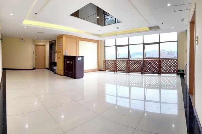A spacious lobby with a high ceiling, a reception desk, and large windows offering a view.