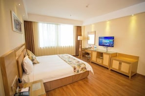 Une chambre d’hôtel avec un lit, un bureau, une télévision et une fenêtre avec des rideaux.