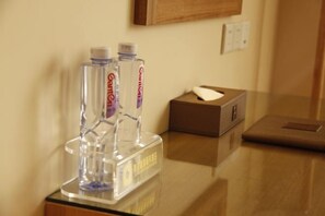 Une chambre d’hôtel avec un distributeur transparent en verre contenant deux bouteilles d’eau, une boîte de mouchoirs et une boîte marron posée sur le comptoir.
