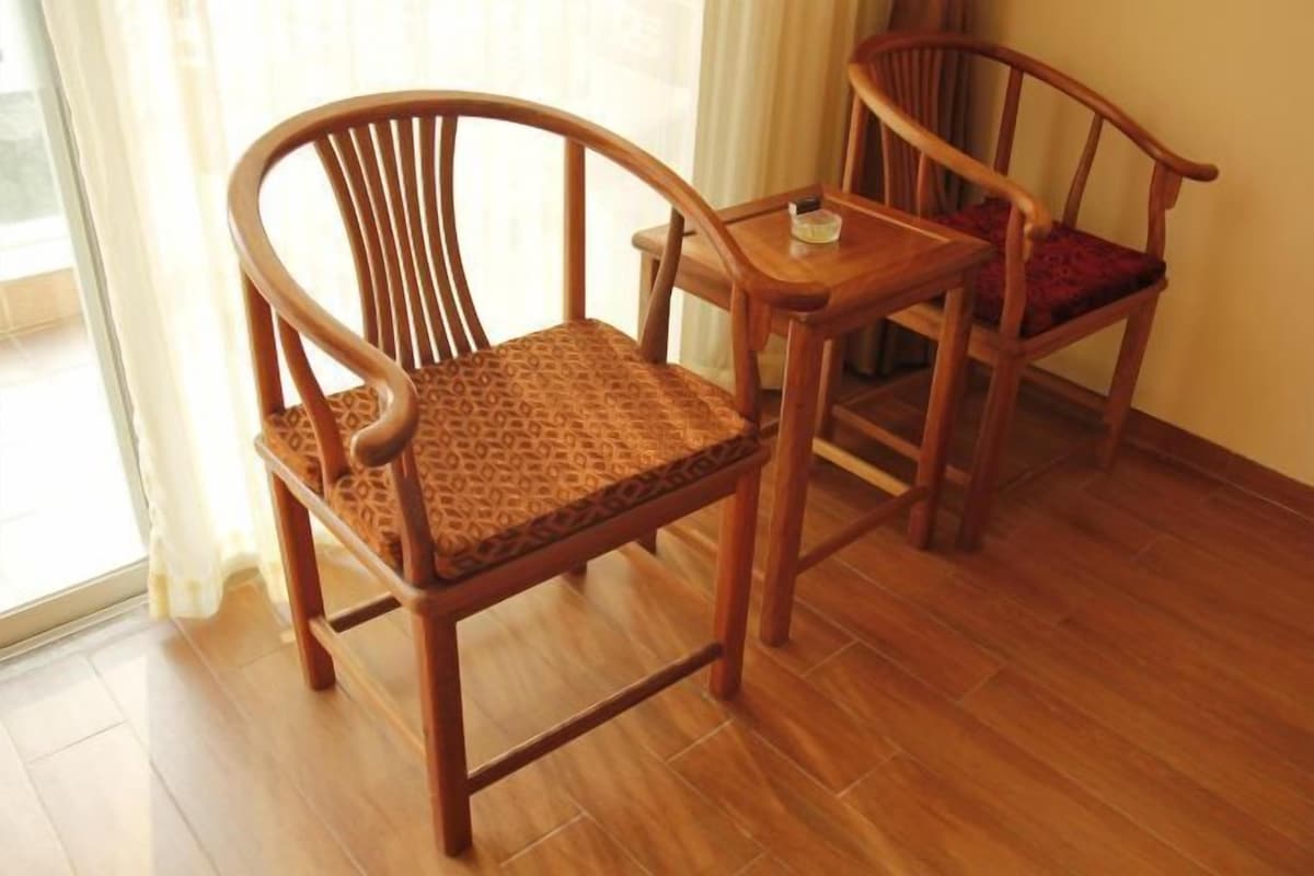 A wooden chair with a patterned cushion and a small wooden table with a red cushion.