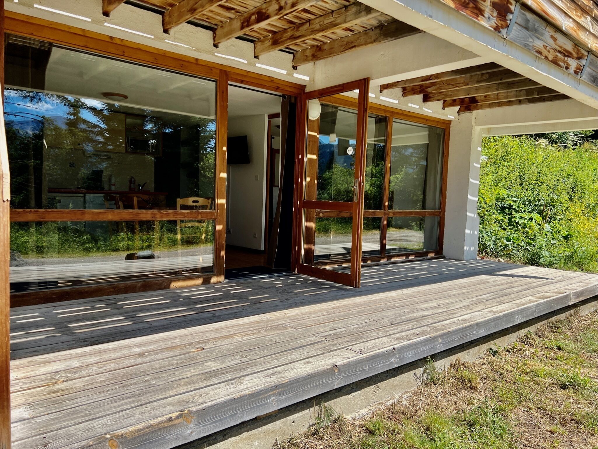 Una casa moderna con puertas de cristal grandes que dan a una terraza de madera.
