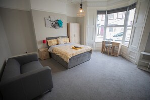 A bedroom with a bed, a desk, a wardrobe, and a sofa.
