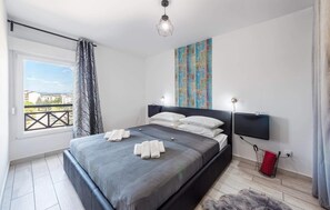 Een moderne slaapkamer met een groot bed, uitzicht door een raam en een stadsgezicht erbuiten.