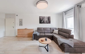 Een moderne woonkamer met een hoekbank, een houten kast en een ronde salontafel.