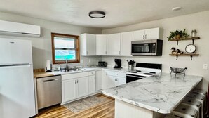A modern kitchen with white cabinets, a built-in microwave, and a large island with stools. - Lakeview Cabin- minutes from beach! (Crofton)