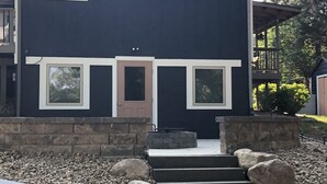 A two-story house with a dark exterior, a front door, and a small porch area. - Lakeview Cabin- minutes from beach! (Crofton)