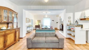 Een ruime woonkamer met een bank, houten kasten en een keukenhoek met planken en apparatuur.