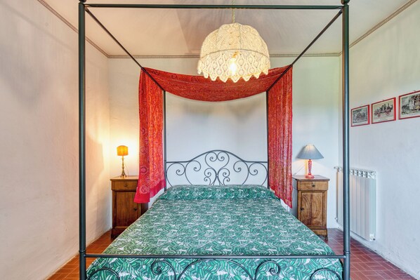 Un lit à baldaquin avec une couvre-lit à motifs verts, des rideaux rouges et un luminaire suspendu.