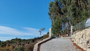 Un sentier pavé de pierres menant en pente raide, bordé de murs de pierre de chaque côté, entouré d’arbres et surplombant un ciel bleu clair.
