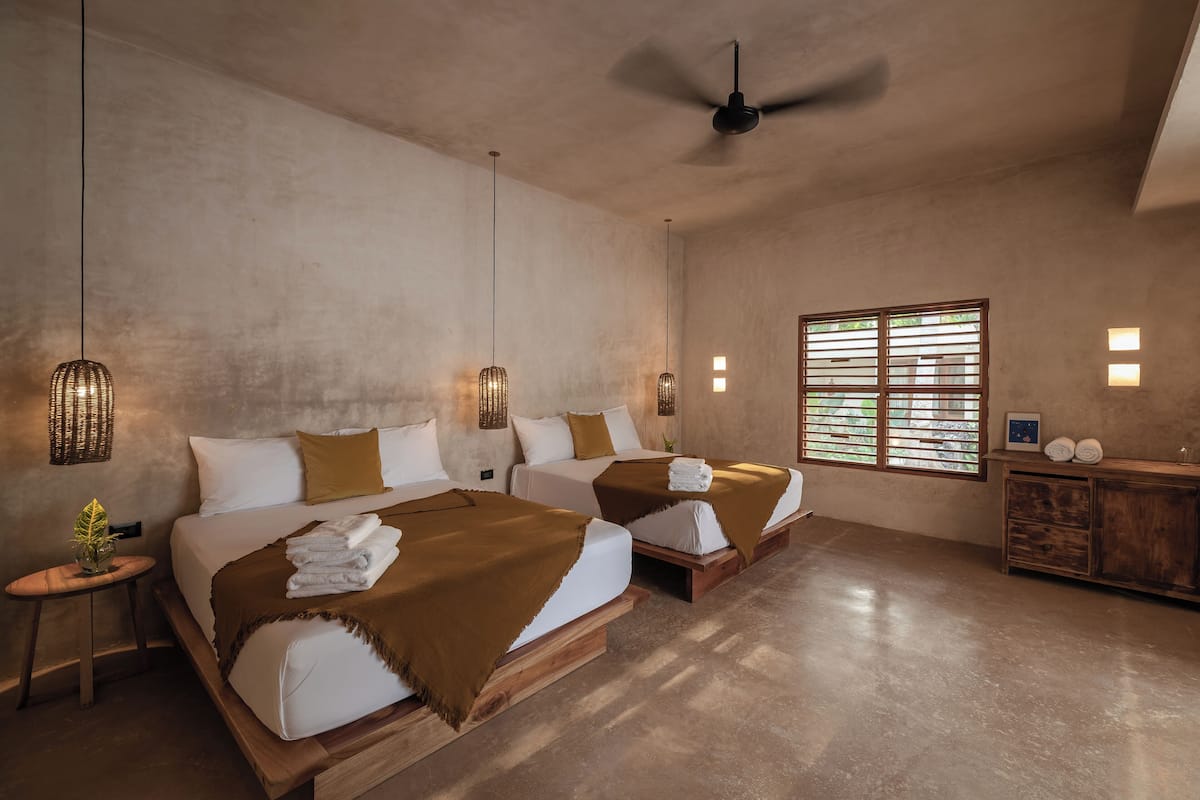 Une chambre d’hôtel avec deux lits, un ventilateur de plafond, une fenêtre avec des stores et une armoire en bois.