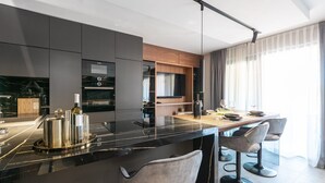 A modern kitchen with dark cabinetry, a black countertop, and a dining area with a wooden table and grey chairs. - Appartment Val di Bora 2 (Porec)