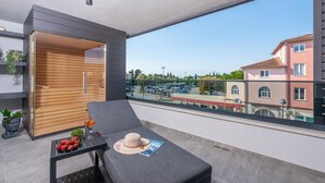 A balcony with a modern design, featuring a grey sofa, a small table with strawberries and a hat, and a view of a parking lot and buildings in the background. - Appartment Val di Bora 2 (Porec)