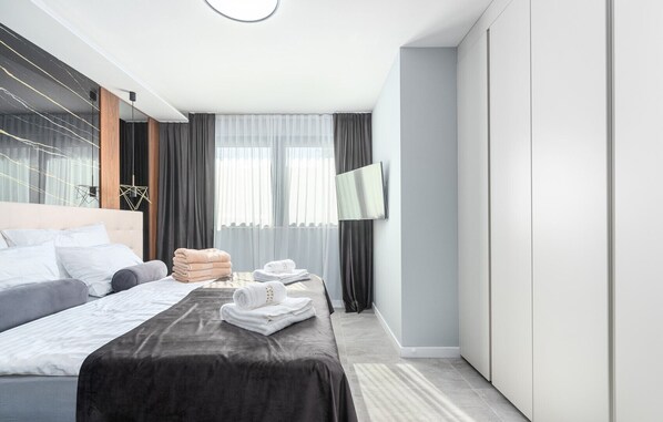 Een moderne hotelkamer met een groot bed, een flatscreen televisie aan de wand en uitzicht op de stad door grote ramen.