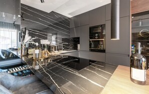 A modern kitchen with a black marble countertop, a built-in oven, and a wine bottle on the counter.