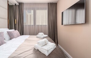 Ein Hotelzimmer mit einem großen Bett, zwei Kissen, einem an der Wand montierten Fernseher und einem Fenster mit Vorhängen.