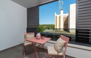 Ein Balkon mit Tisch und zwei Stühlen, einem Blumentopf und Blick auf ein Gebäude mit einem Sendeturm.