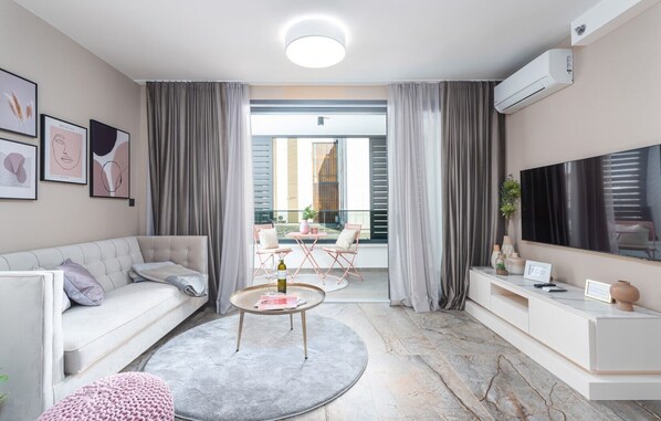 Ein modernes Wohnzimmer mit Sofa, Couchtisch und Fernseher. Ein Balkon mit Tisch und Stühlen ist ebenfalls vorhanden.
