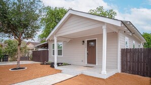 A single-story house with a covered porch, a front door, and a small front yard with a tree and a fence.