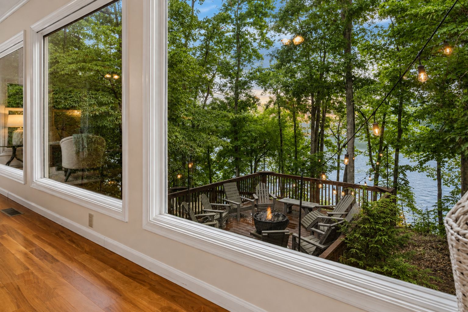 A wooden deck with outdoor seating and a fire pit, overlooking a lake with trees.