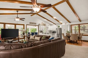 A spacious living room with a large leather sectional sofa, a flat-screen TV, and a ceiling fan.