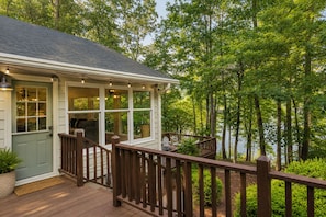 A wooden deck with a railing, a covered porch with windows, and a view of a lake surrounded by trees. - Shoreline Landing with Dock! (Toccoa)