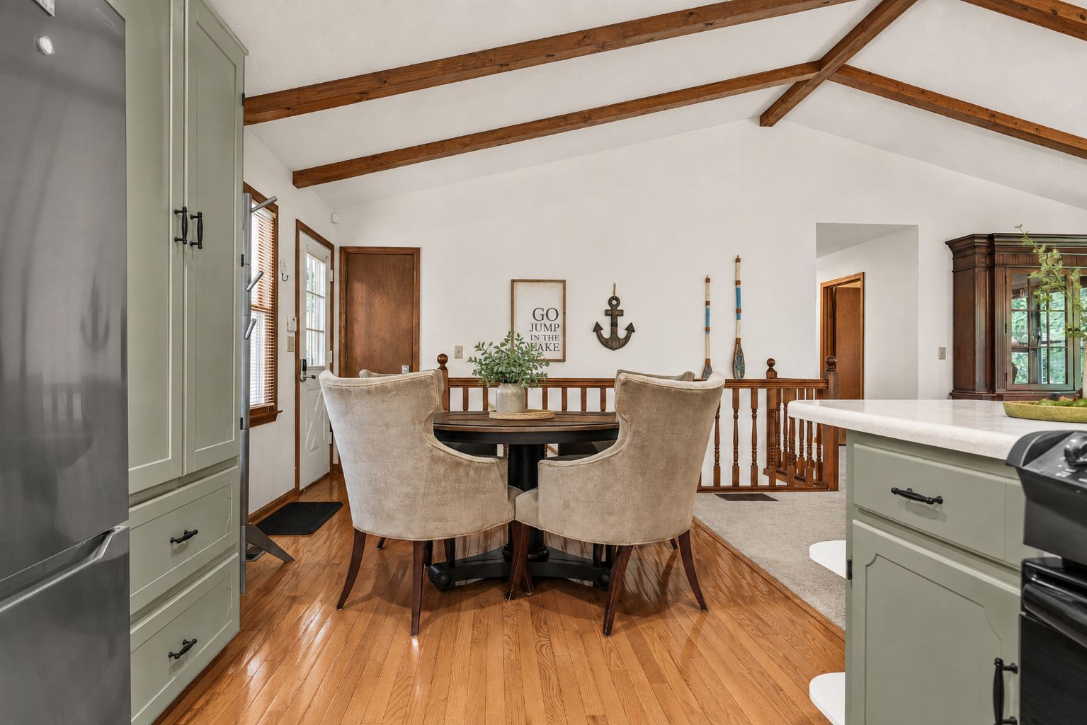 Un comedor con mesa y sillas de madera, una cocina con armarios y un techo con vigas a la vista.