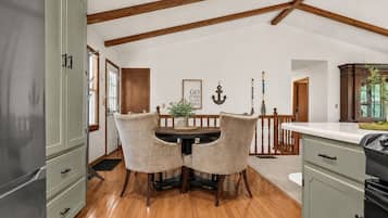 Un comedor con mesa y sillas de madera, una cocina con armarios y un techo con vigas a la vista.