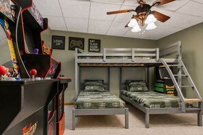 A bunk bed room with a ceiling fan, framed posters on the wall, and a gaming console.