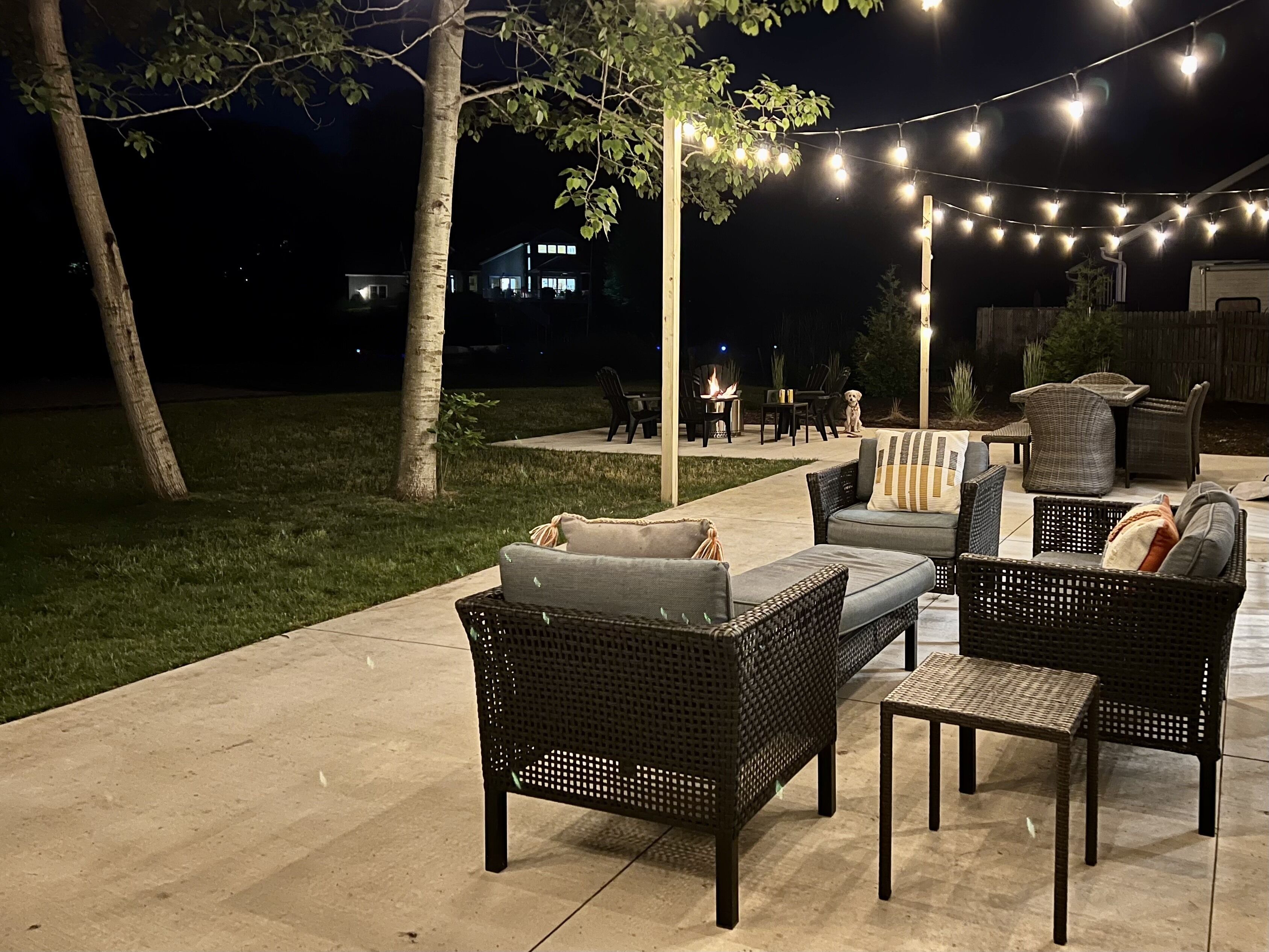 An outdoor patio area with wicker furniture, string lights, and a fire pit.