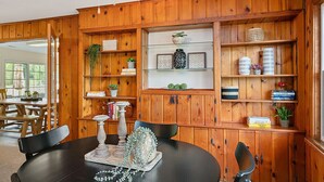 Un coin repas avec une table ronde, des chaises et un mur en lambris de bois agrémenté d’étagères où sont disposés des livres, des plantes et des objets décoratifs.