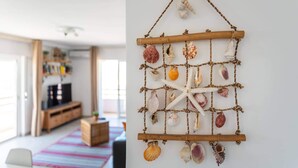 A room with a wooden entertainment unit, a colorful striped rug, and a wall-mounted decorative piece with seashells and a starfish. - Faro Center Stunning View (Faro)