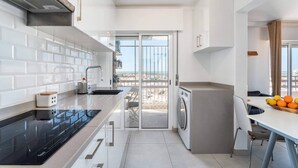 A modern kitchen with a built-in stove, a washing machine, and a dining area with a view. - Faro Center Stunning View (Faro)