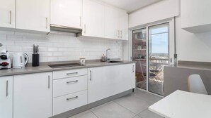 A modern kitchen with white cabinets, a built-in oven, and a window overlooking a balcony. - Faro Center Stunning View (Faro)