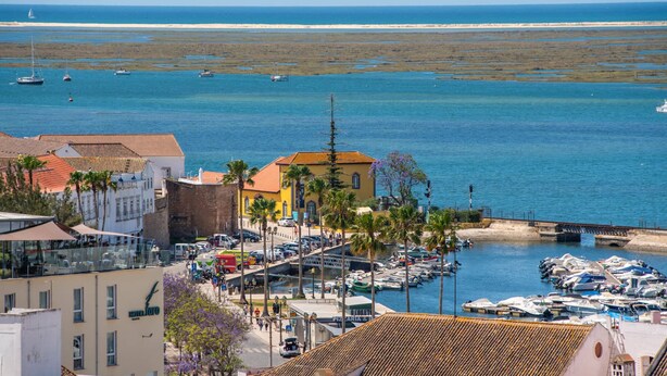 A coastal town with a marina, buildings with red-tiled roofs, and a sandy beach in the background. - Faro Center Stunning View (Faro)