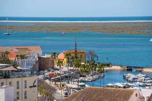 Un pueblo costero con un puerto deportivo, edificios con tejados rojos y una playa de arena al fondo.