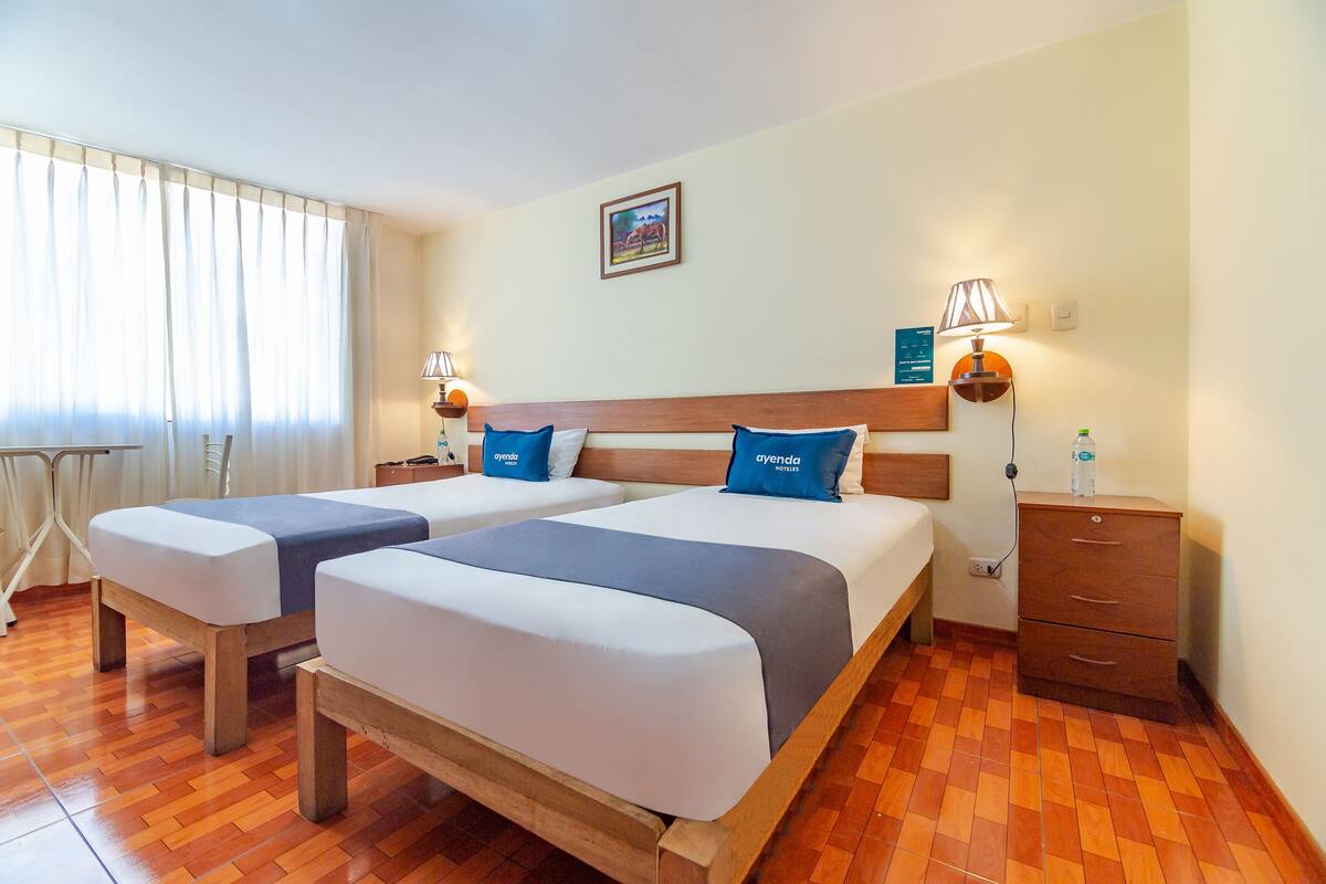 Ein Hotelzimmer mit zwei Betten, Holzkopfteilen und einem Nachttisch mit einer Lampe.