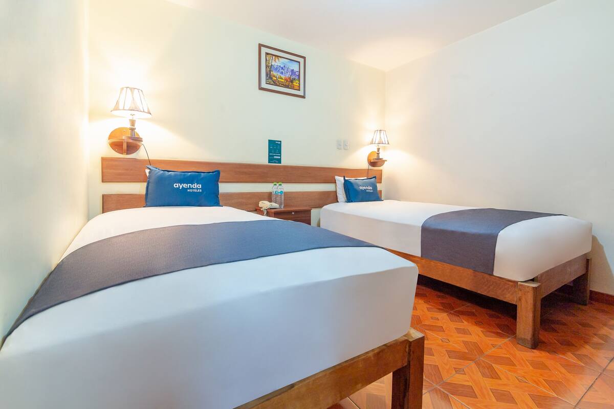 Ein Hotelzimmer mit zwei Betten, jeweils mit einem hölzernen Kopfteil, einem Nachttisch und einer Lampe.