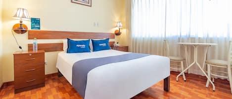 A hotel room with a bed, two bedside tables, a desk, and chairs.
