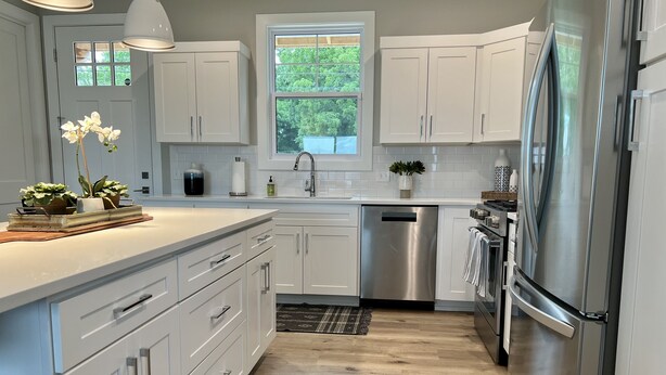 A modern kitchen with white cabinets, stainless steel appliances, and a window providing natural light.