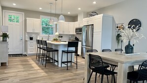 A modern kitchen with white cabinets, a stainless steel refrigerator, and a dining area with black chairs and a wooden table.