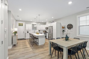 A modern kitchen with a central island, white cabinetry, stainless steel appliances, and a dining area with a wooden table and black chairs. - New Saugatuck Home: Lake Views & Walk to Town (Douglas)