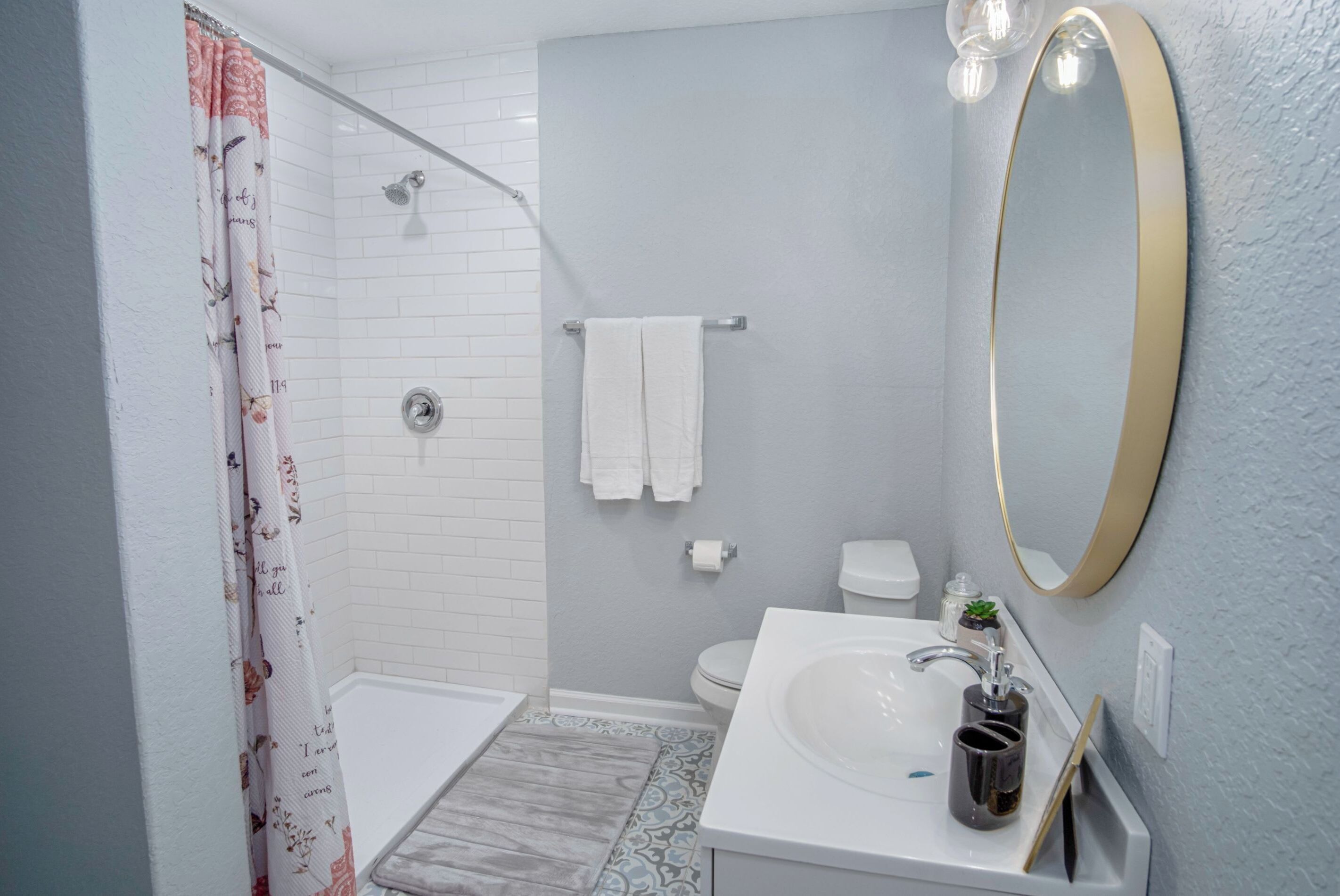 A bathroom with a shower, toilet, sink, and a large mirror.