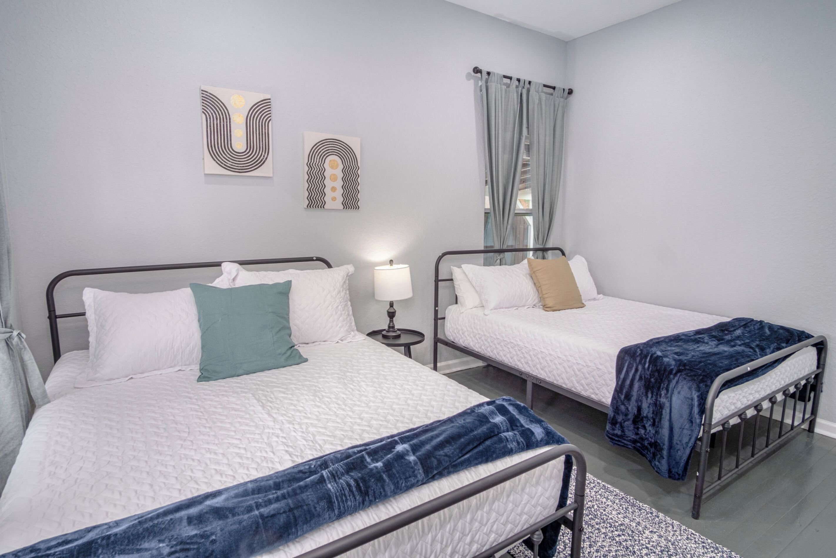 Une chambre d’hôtel avec deux lits, une table de chevet avec une lampe et une fenêtre avec des rideaux.
