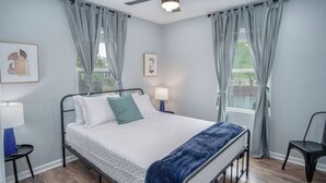 Ein Schlafzimmer mit einem Bett, zwei Nachttischen mit Lampen, einem Deckenventilator und hellen Vorhängen.