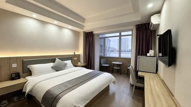 A hotel room with a bed, bedside tables, a desk, a chair, a TV, and a window with curtains.