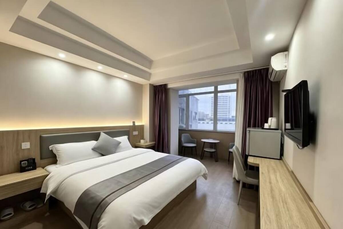 Ein Hotelzimmer mit Bett, Nachttischen, Schreibtisch, Stuhl, Fernseher und einem Fenster mit Vorhängen.