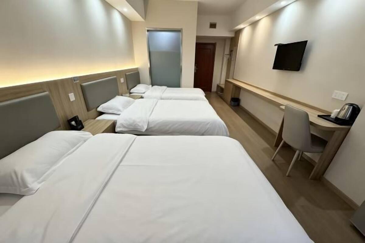 Ein Hotelzimmer mit drei Betten, einem Schreibtisch, einem Stuhl, einem Fernseher und einer Tür.
