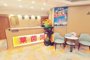 Un espace d’accueil d’hôtel comprenant un comptoir de réception, deux chaises, une petite table et une affiche accrochée au mur.
